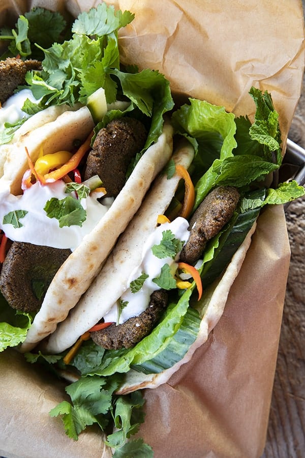 Top view of falafel in flatbread with pickled vegetables, lettuce, yogurt, cilantro, on brown paper.