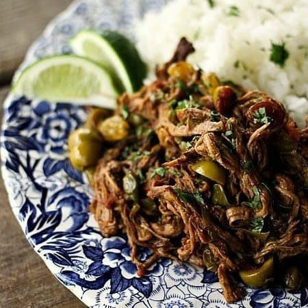 Ropa Vieja: Thin shreds of braised flank steak, olives, capers, tomatoes, lime wedges, long grain white rice, parsley, on an antique blue and white plate