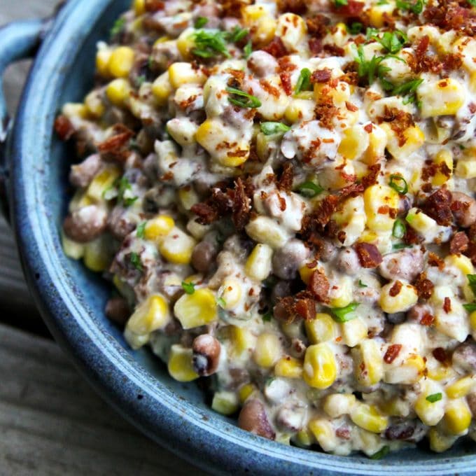 Slow-Cooker Black-Eyed Pea Dip with Corn and Bacon in blue speckled pottery bowl, sliced green onions, crumbled bacon, black eyed peas, corn, in a creamy sauce
