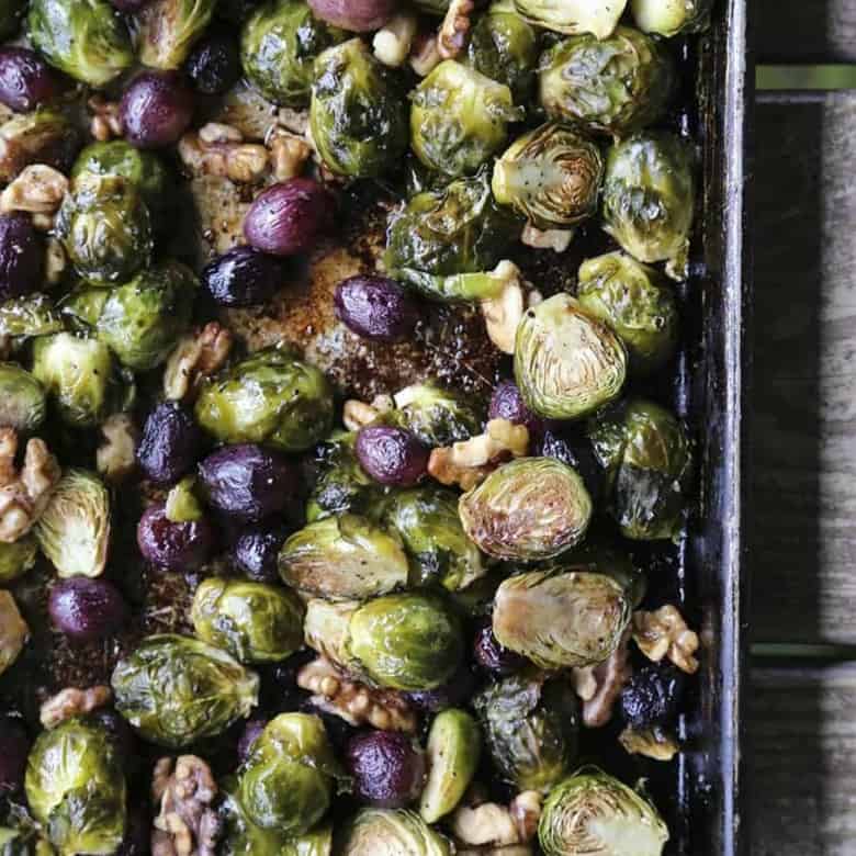 Roasted Brussels Sprouts with Walnuts and Grapes on antique metal sheet pan, wooden table, maldon sea salt
