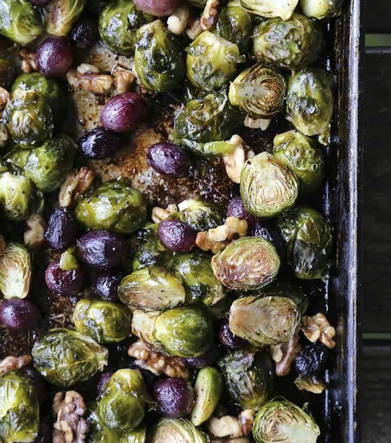 Roasted Brussels Sprouts with Walnuts and Grapes on antique metal sheet pan, wooden table, maldon sea salt