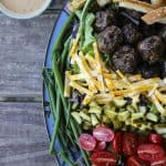 Cheeseburger Salad from foodiewithfamily.com with sesame bun croutons. grilled meatballs and green onions, cheese, pickles, tomatoes, and hot fries.