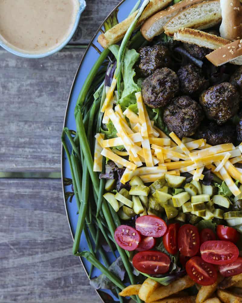 Cheeseburger Salad from foodiewithfamily.com with sesame bun croutons. grilled meatballs and green onions, cheese, pickles, tomatoes, and hot fries.