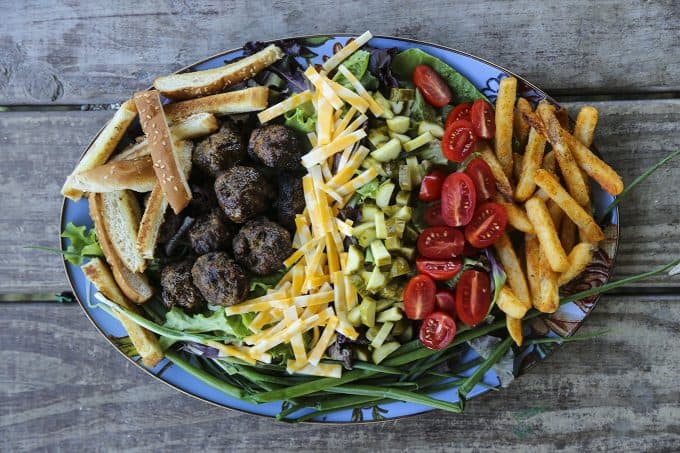 Cheeseburger Salad from foodiewithfamily.com with sesame bun croutons. grilled meatballs and green onions, cheese, pickles, tomatoes, and hot fries.