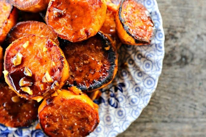 Melting Sweet Potatoes with sauce and garlic, roasted sweet potato rounds, caramelized, blue and white plate, on rustic wood table