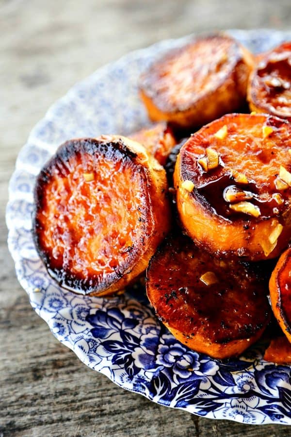 Melting Sweet Potatoes with sauce and garlic, thick roasted sweet potato rounds, caramelized, blue and white plate, on rustic wood table