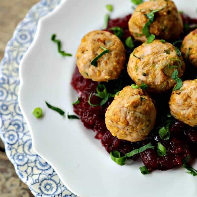 Turkey and stuffing meatballs, cranberry sauce, white target plate on antique blue and white scallopped plate, wooden background, 3/4 view, chopped parsley and green onions
