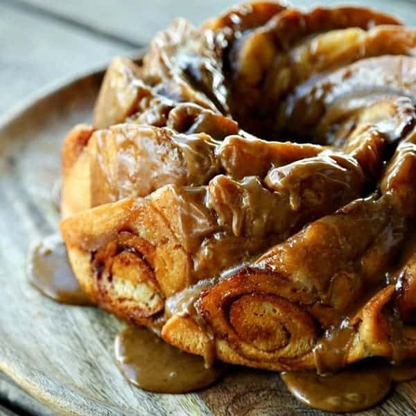 Cinnamon Roll Coffee Cake on round wooden cake plate, coffee glaze dripping, bundt pan scallops