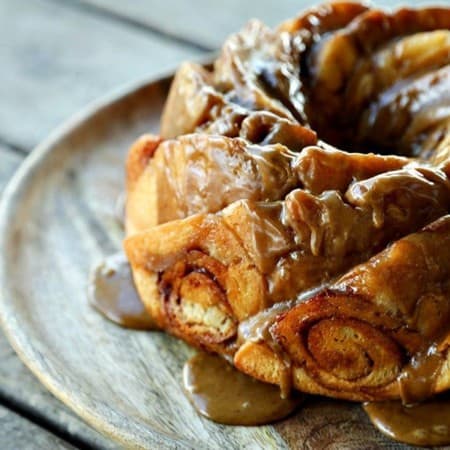 Cinnamon Roll Coffee Cake in bundt pan scallops, dripping coffee glaze, round wooden cake plate, wooden table