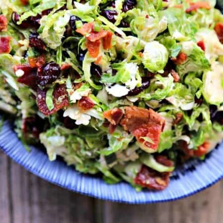 Cranberry Brussels Salad with Bacon Vinaigrette: shredded brussels sprouts, crisp bacon, dried cranberries, craisins, blue and white oval serving bowl, wooden background