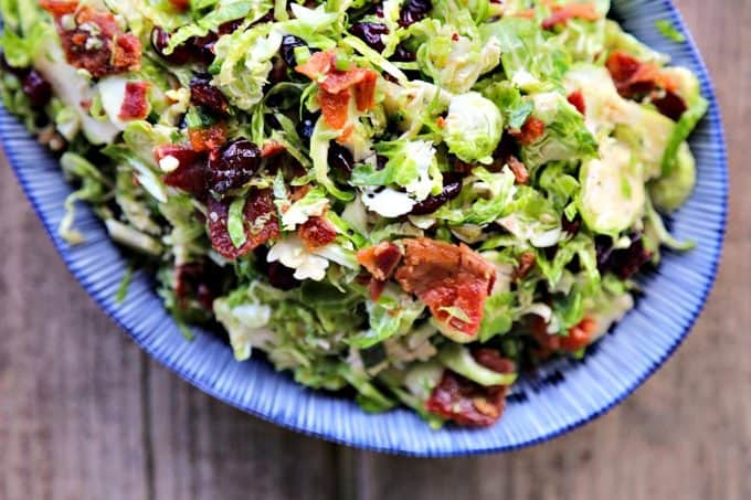 Cranberry Brussels Salad with Bacon Vinaigrette: shredded brussels sprouts, crisp bacon, dried cranberries, craisins, blue and white oval serving bowl, wooden background