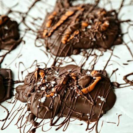 Chocolate Covered Caramel Stuffed Pretzels drizzled with caramel candy, chocolate, maldon sea salt flakes on parchment paper