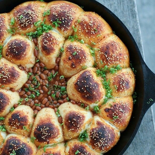 Cheeseburger Bombs Baked Bean Skillet, sesame topped rolls stuffed with meatballs, arranged in circles around baked beans, cast iron skillet, sliced green onions