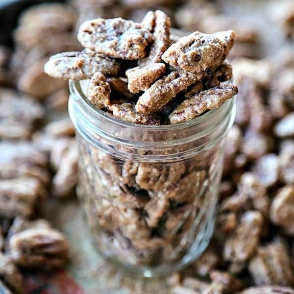 Candied Maple Pecans in a half pint glass jar surrounded by more candied pecans
