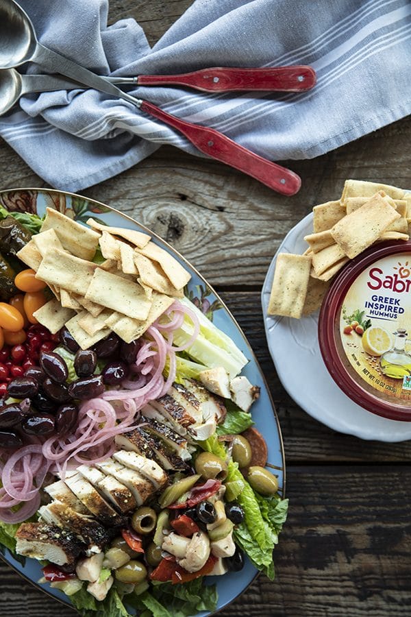 Greek Salad with lemon garlic chicken, marinated olive salad, quick pickled red onions, crumbled feta cheese, garlic stuffed kalamata olives, tiny grape tomatoes, stuffed grape leaves, Greek salad dressing, pita chips as croutons, and a hearty dollop of hummus. This salad will fill you up with sunshiny goodness without making you feel like a slug. The post includes instructions on how to pack these salads up to four days ahead of time for work-week and school lunches.