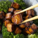 Crispy, golden brown cubes of air fryer tofu served with a drizzle of honey and broccoli on a blue and white striped oblong bowl.