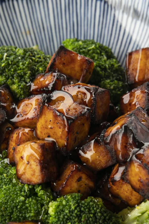 Crispy, golden brown cubes of air fryer tofu served with a drizzle of honey and broccoli on a blue and white striped oblong bowl.