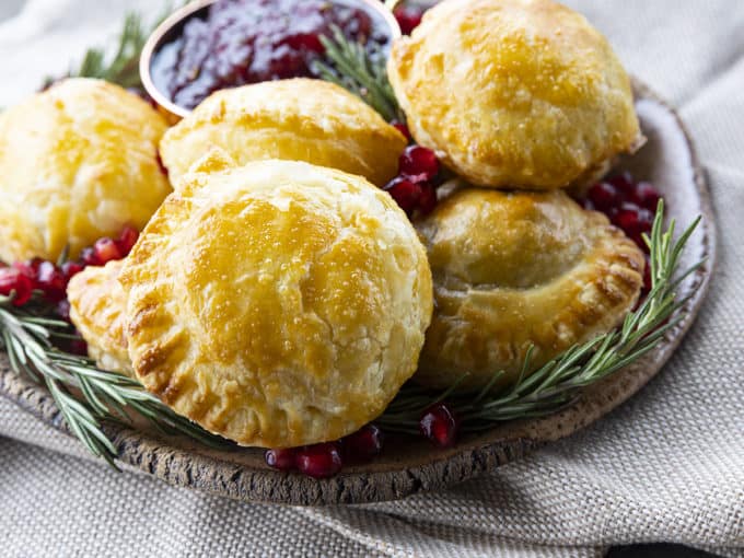 Bite sized baked brie in puff pastry with rosemary, pomegranate seeds, and sweet and spicy cranberry sauce.