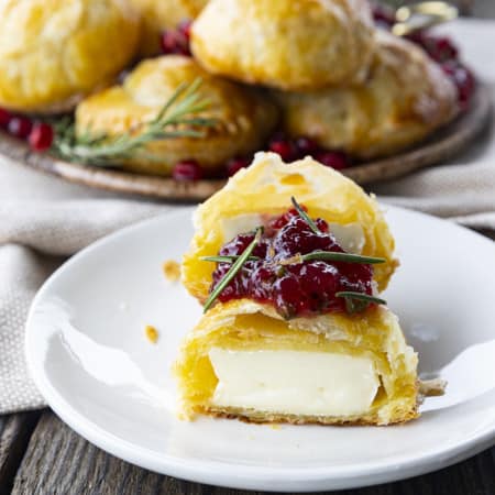 Bite sized baked brie in puff pastry with rosemary, pomegranate seeds, and sweet and spicy cranberry sauce.
