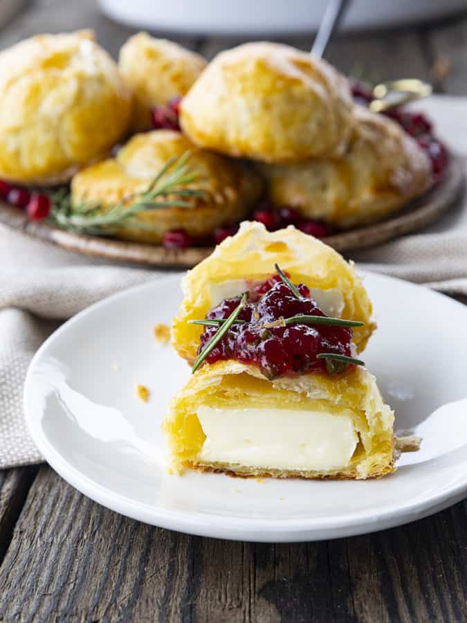 Bite sized baked brie in puff pastry with rosemary, pomegranate seeds, and sweet and spicy cranberry sauce.