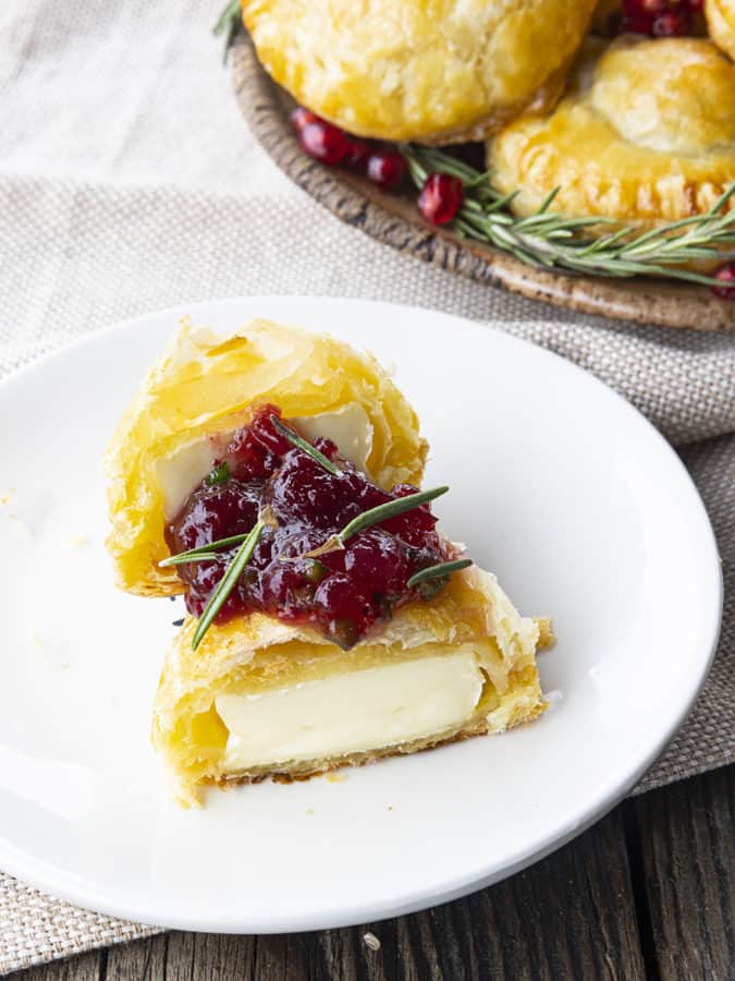 Bite sized baked brie in puff pastry with rosemary, pomegranate seeds, and sweet and spicy cranberry sauce.