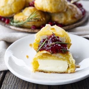 Bite sized baked brie in puff pastry with rosemary, pomegranate seeds, and sweet and spicy cranberry sauce.