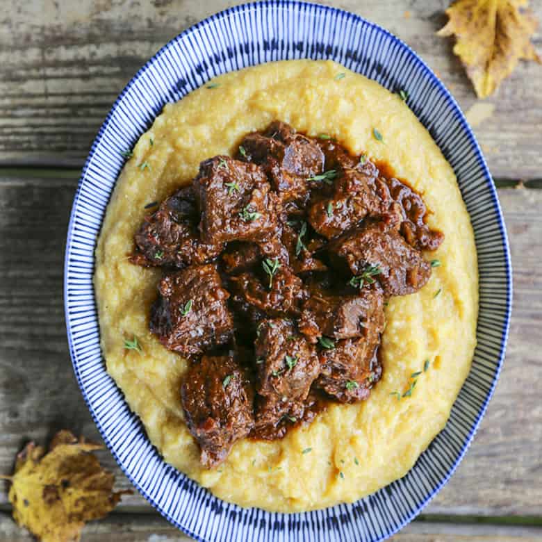 Tuscan Braised Beef in red wine sauce on creamy polenta in a blue and white dish.