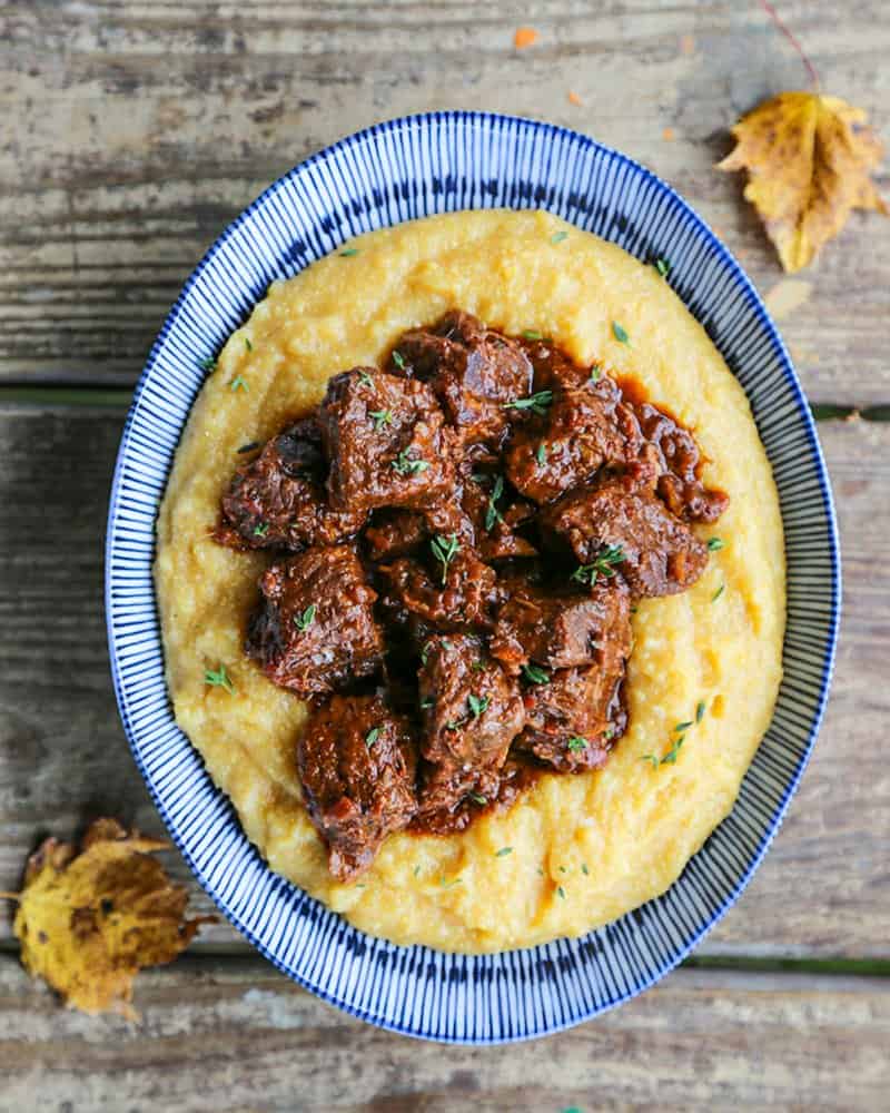Tuscan Braised Beef in red wine sauce on creamy polenta in a blue and white dish.