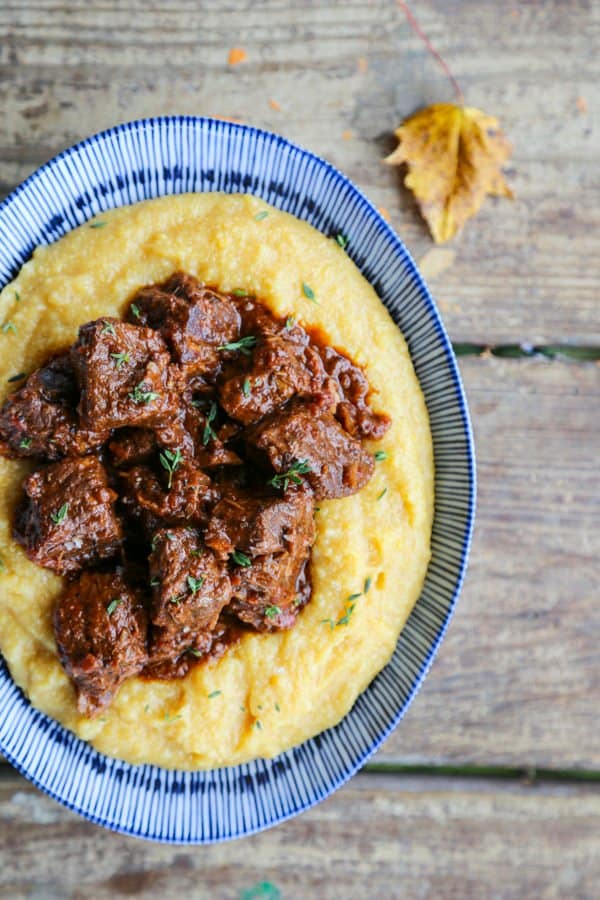 Tuscan Braised Beef in red wine sauce on creamy polenta in a blue and white dish.