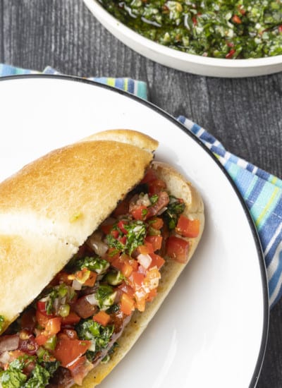 Choripan: Garlicky, spicy, smoky chorizo sausage is slowly grilled to perfection before being split, seared over high heat, and served on a bun with fresh chimichurri sauce and salsa a la criolla; the messier the better!