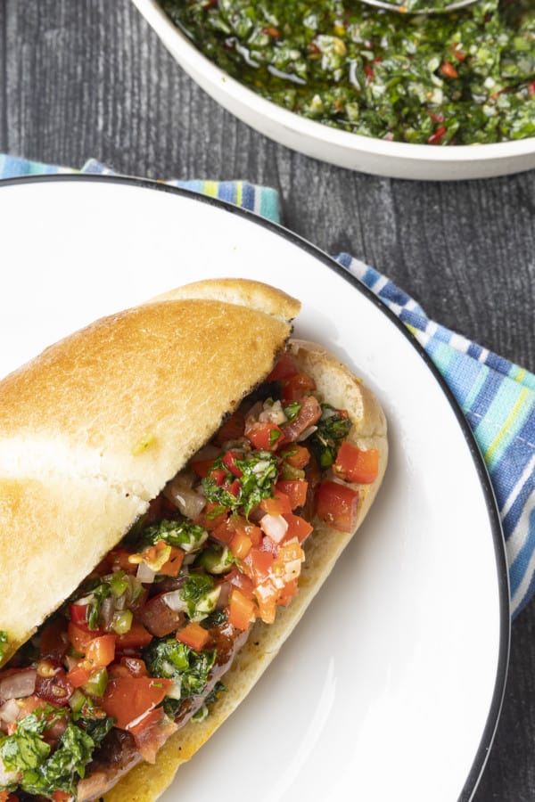 Choripan: Garlicky, spicy, smoky chorizo sausage is slowly grilled to perfection before being split, seared over high heat, and served on a bun with fresh chimichurri sauce and salsa a la criolla; the messier the better!