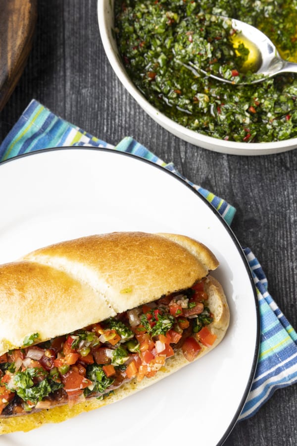 Choripan: Garlicky, spicy, smoky chorizo sausage is slowly grilled to perfection before being split, seared over high heat, and served on a bun with fresh chimichurri sauce and salsa a la criolla; the messier the better!