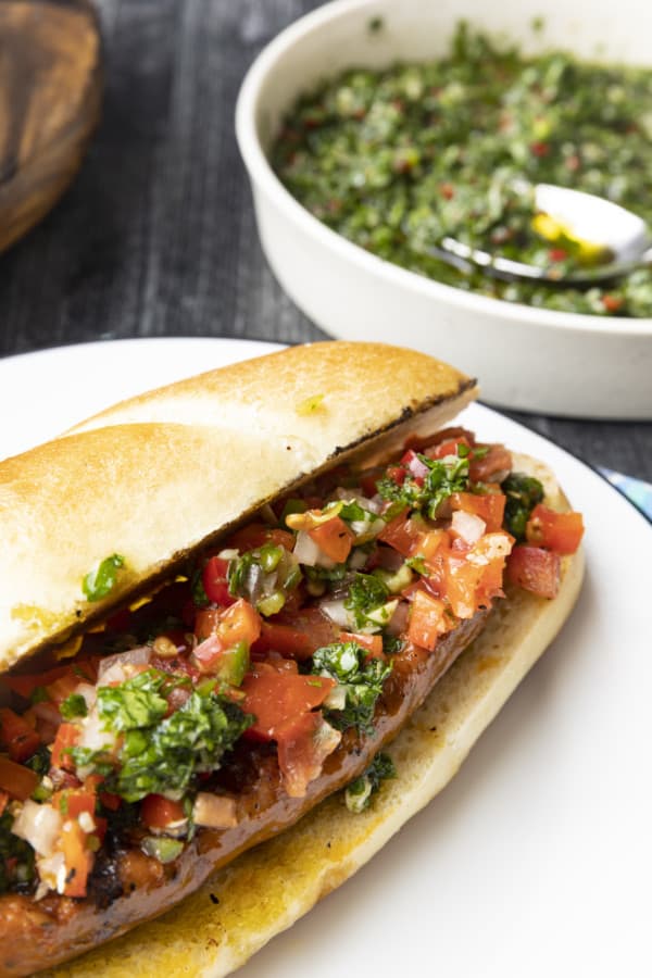 Choripan: Garlicky, spicy, smoky chorizo sausage is slowly grilled to perfection before being split, seared over high heat, and served on a bun with fresh chimichurri sauce and salsa a la criolla; the messier the better!