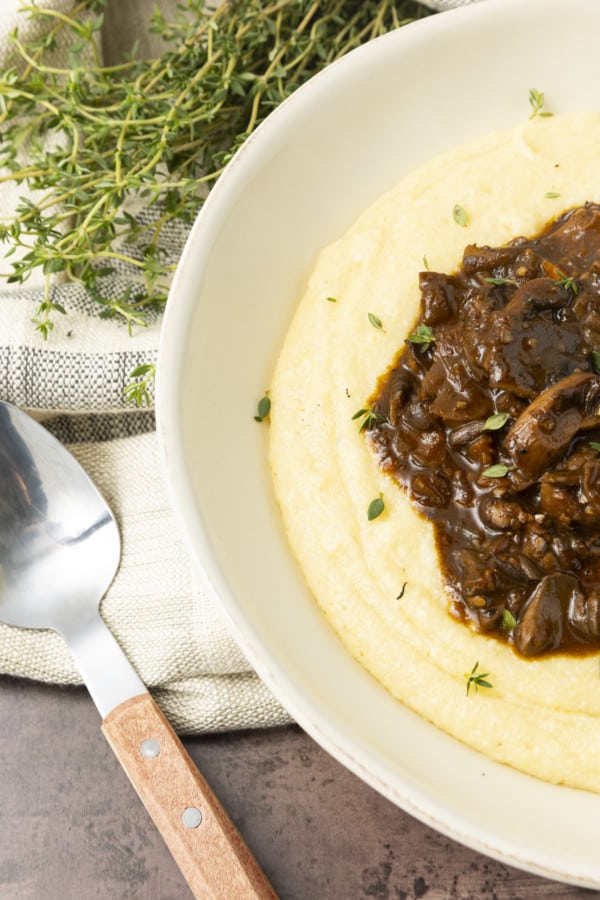 Mushroom stew over polenta in a pottery bowl with thyme nearby.