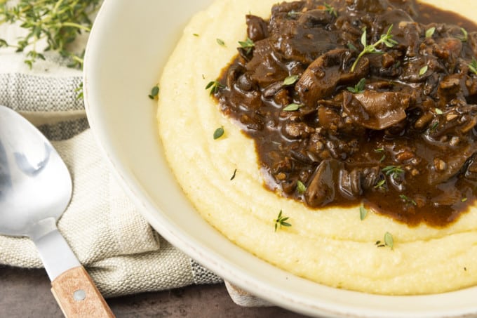 Mushroom stew over polenta in a pottery bowl with thyme nearby.