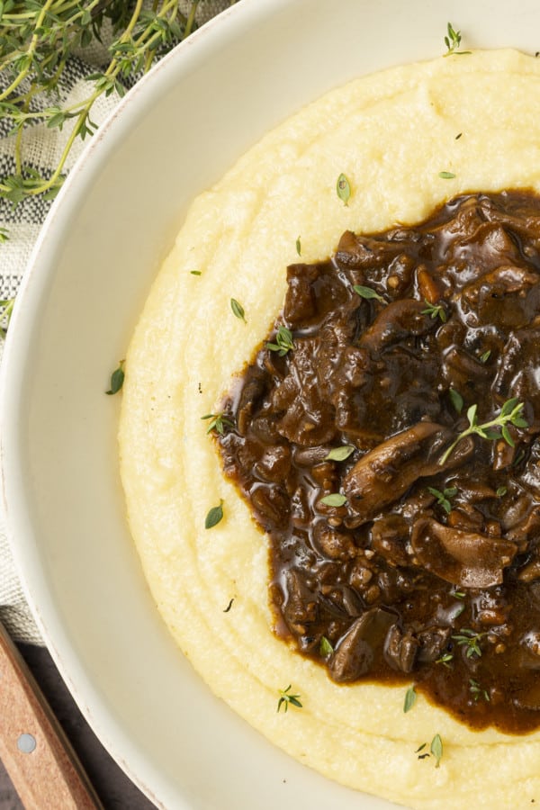 Mushroom stew over polenta in a pottery bowl with thyme nearby.