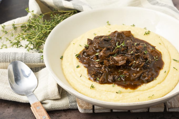 Mushroom stew over polenta in a pottery bowl with thyme nearby.