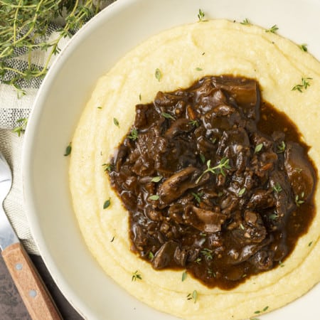 Mushroom stew over polenta in a pottery bowl with thyme nearby.