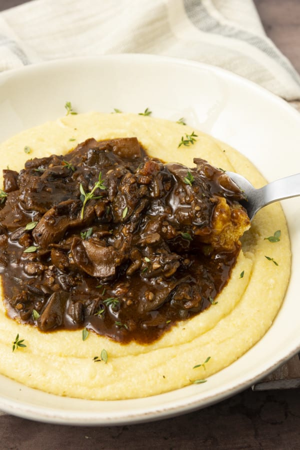 Mushroom stew over polenta in a pottery bowl with thyme nearby.