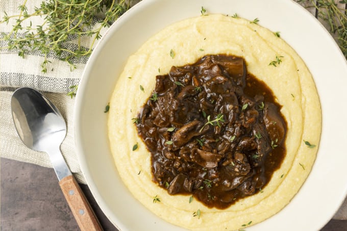 Mushroom stew over polenta in a pottery bowl with thyme nearby.