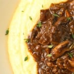 Mushroom stew over polenta in a pottery bowl with thyme nearby.