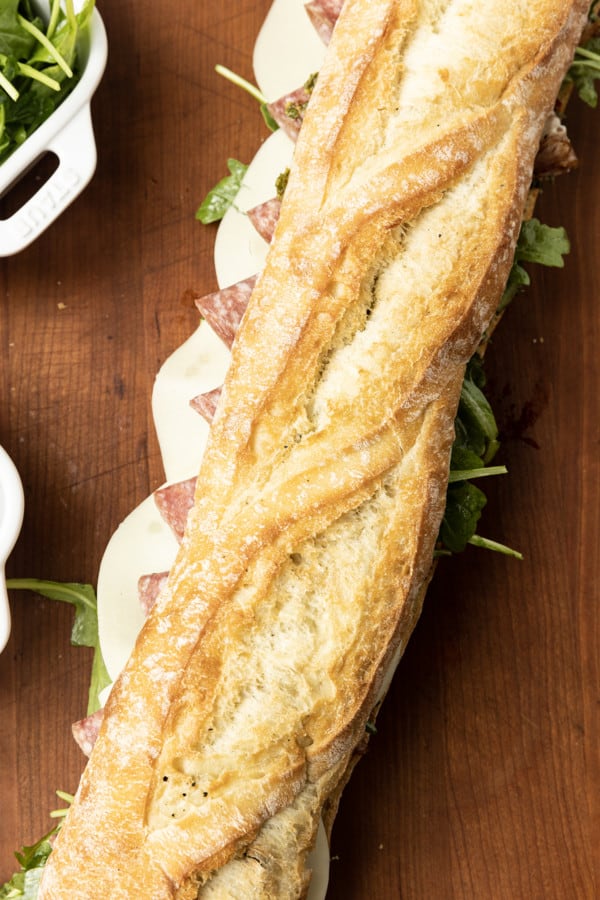 This is no ordinary Salami Sandwich; a crusty baguette is stuffed to bursting with a variety of salamis, roasted red pepper, pesto sauce, provolone cheese, fresh basil, and dressed arugula, then tightly wrapped and stashed in the refrigerator overnight. Then you can slice it all up and arrange it on a platter for a party or stretch it out for up to 5 days! And let me tell you, if you slice a little off of this every day for lunch with a cup of soup or bag of chips, you're going to feel very clever indeed. If you're feeling generous, pop it in a lunch bag for a school lunch that will make your kid the envy of the school.