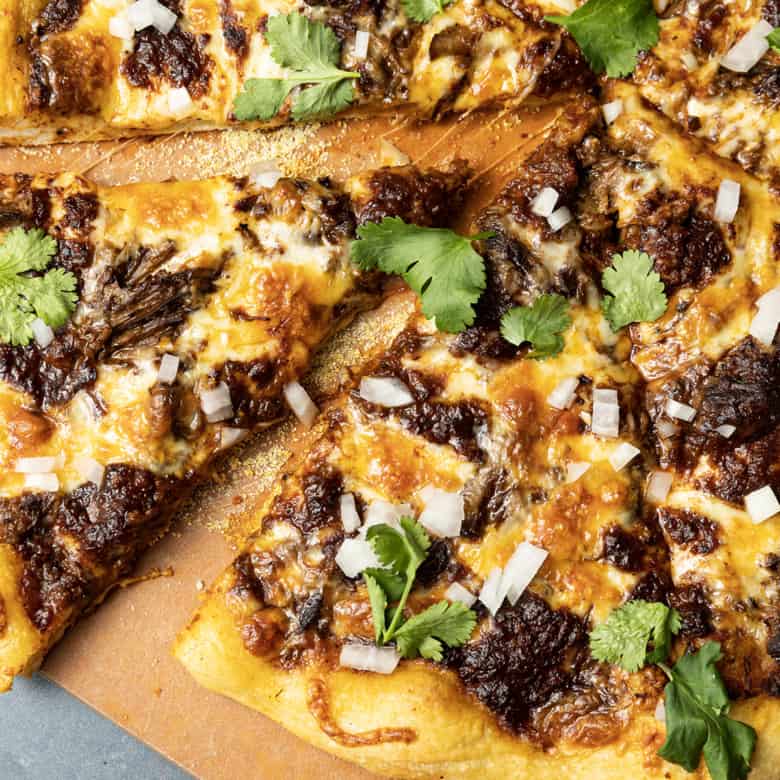 Birria Pizza: Chewy crust topped with tender shredded birria beef, smoky birria stew, loads of melted cheese, chopped sweet onion, fresh cilantro, a squeeze of fresh lime, and a bowl of red chile sauce for dipping. Imagine the best tacos you’ve ever tasted turned into a pizza and you have an idea just how fabulous this pizza is.