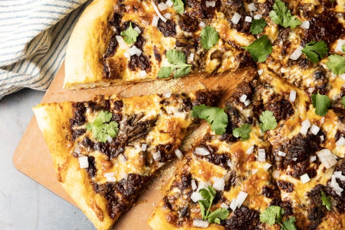Birria Pizza: Chewy crust topped with tender shredded birria beef, smoky birria stew, loads of melted cheese, chopped sweet onion, fresh cilantro, a squeeze of fresh lime, and a bowl of red chile sauce for dipping. Imagine the best tacos you’ve ever tasted turned into a pizza and you have an idea just how fabulous this pizza is.