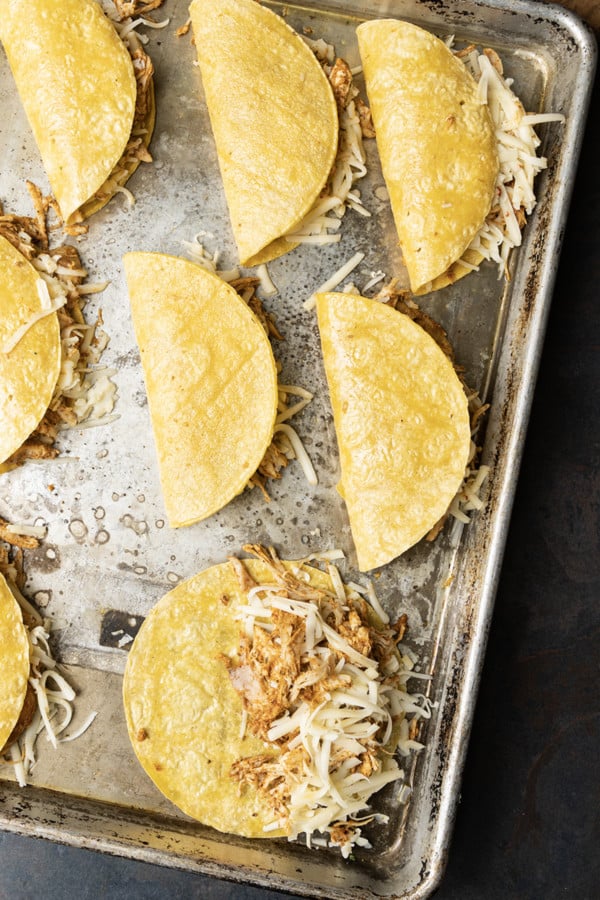 Ridiculously easy Crispy Chicken Tacos are the best of tacos, taquitos, and nachos combined! Flavourful shredded chicken and scandalous amounts of melted cheese are baked in corn tortillas until crispy, crunchy and altogether irresistible! This is bound to be your new favourite for busy weeknight meals, friends.