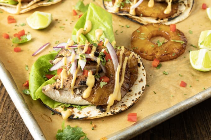 Make taco nights magical with jerk chicken tacos! Fresh lettuce leaves stacked on charred tortillas are piled high with juicy jerk chicken, grilled pineapple slices, diced bell peppers, thinly sliced onions, a drizzle of sauce or spoonful of mango salsa.