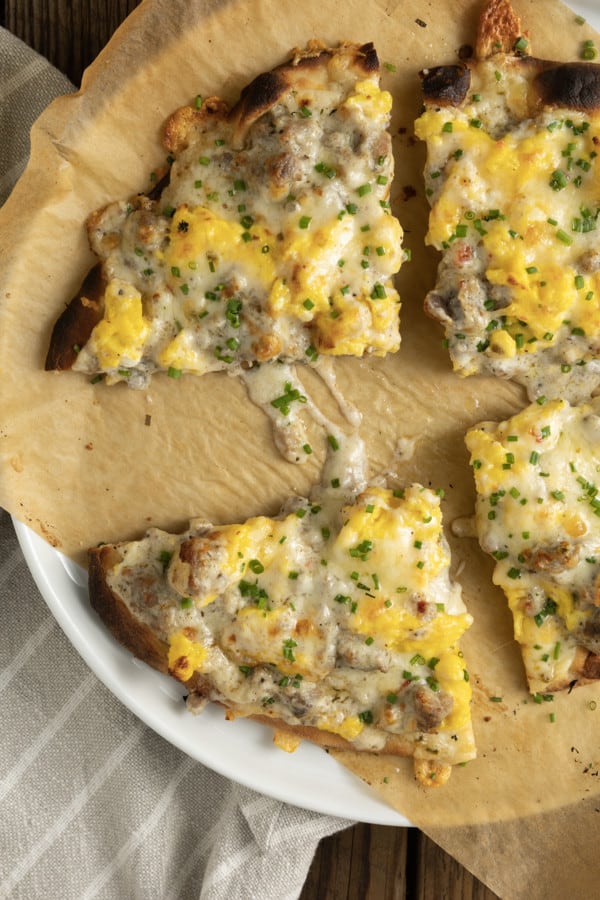 Hold onto your socks, because Sausage Gravy Breakfast Pizza just might knock them off! This ultimate comfort food mashup is coming soon to a breakfast, brunch (or dinner!) table near you. Chewy pizza crust is topped with cheesy, fluffy scrambled eggs, savoury, flavourful, creamy sausage gravy, and fragrant chives in this deliciously different pizza. Made on naan bread (or pre-baked pizza shells, homemade or purchased), these pizzas come together in just moments, too!