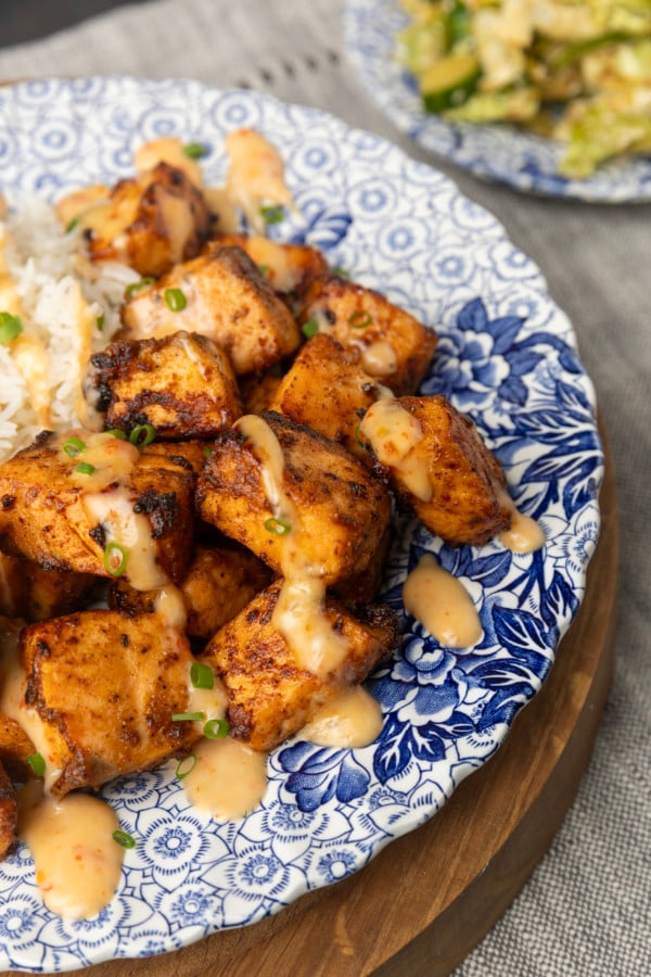crispy air fryer bang bang salmon bites drizzled with sauce served with ice on a blue and white floral plate