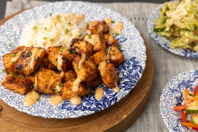 crispy air fryer bang bang salmon bites drizzled with sauce served with ice on a blue and white floral plate