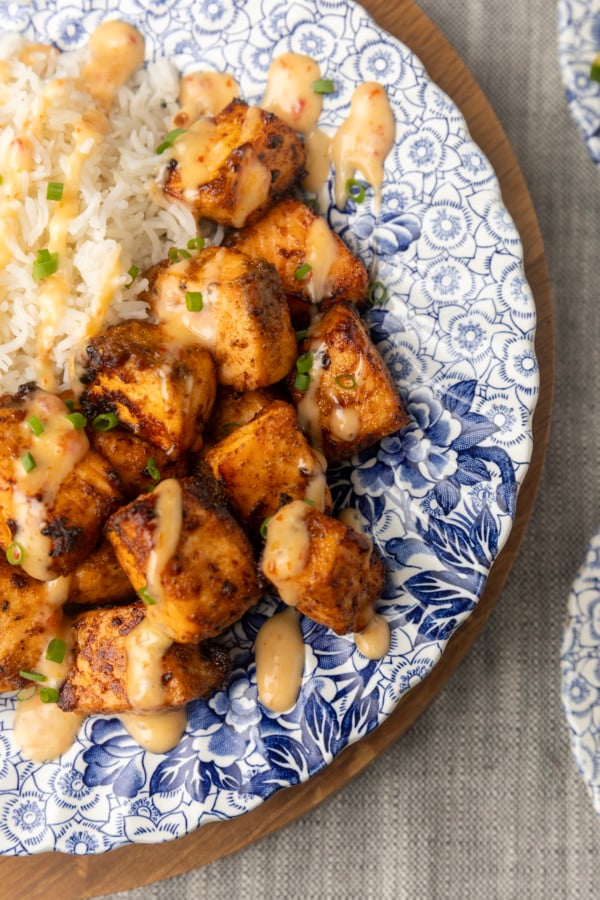 crispy air fryer bang bang salmon bites drizzled with sauce served with ice on a blue and white floral plate